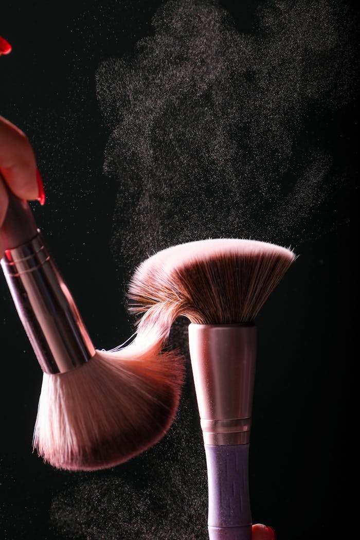 Close-up of makeup brushes with powder cloud against a dark studio background, showcasing movement.