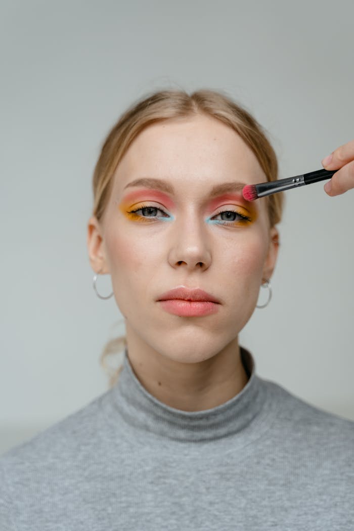 Close-up portrait of a woman applying colorful eyeshadow makeup.