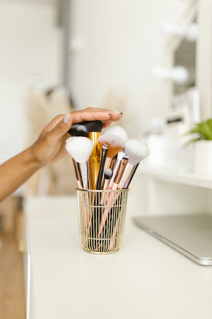 Elegant photo of a hand reaching for a variety of makeup brushes in a holder, ideal for beauty and lifestyle themes.